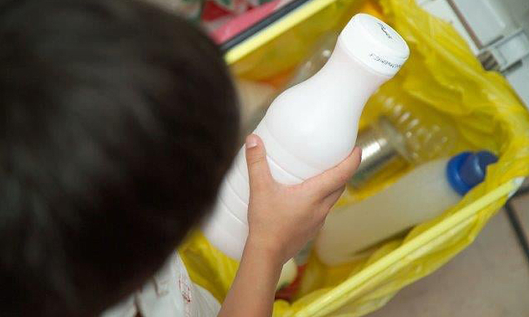 Niño depositando en contenedor amarillo un envase de plástico